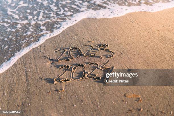 2024 start of the year writting in the sand sandand end of 2023 on the beach at sunset - start of year stock pictures, royalty-free photos & images