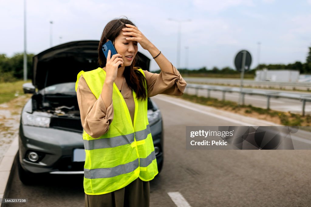 Young woman with reflective west calling help for her broken vehicle on highway