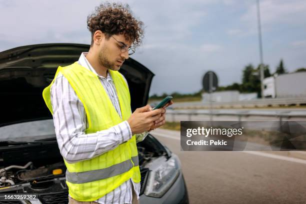 giovane uomo con messaggi di testo occidentali riflessivi per chiedere aiuto per il suo veicolo rotto sull'autostrada - vehicle breakdown foto e immagini stock