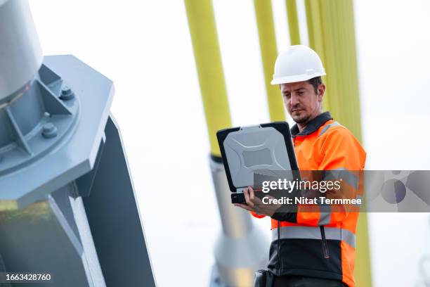 centralized document management system can help and support field operations in the construction industry. a project manager uses a laptop to review project planning and order tasks via cloud-based while standing next to a cable-stayed bridge construction - centralized technology stock pictures, royalty-free photos & images