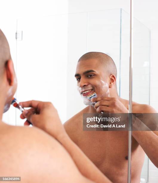 man shaving in bathroom mirror - man shaving face stock-fotos und bilder