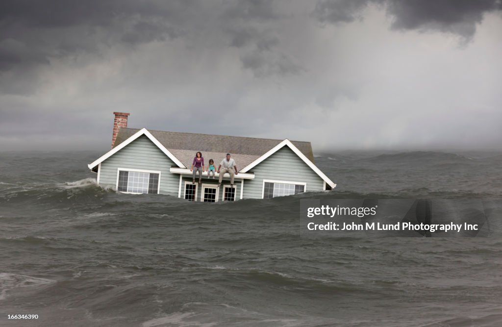 Family sitting on roof of house floating in sea