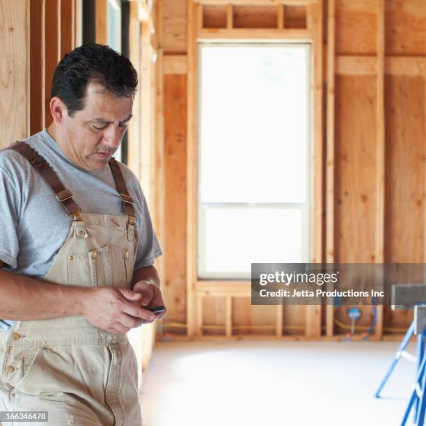 hispanic construction worker text messaging on cell phone in unfinished room - regarder vers le bas photos et images de collection