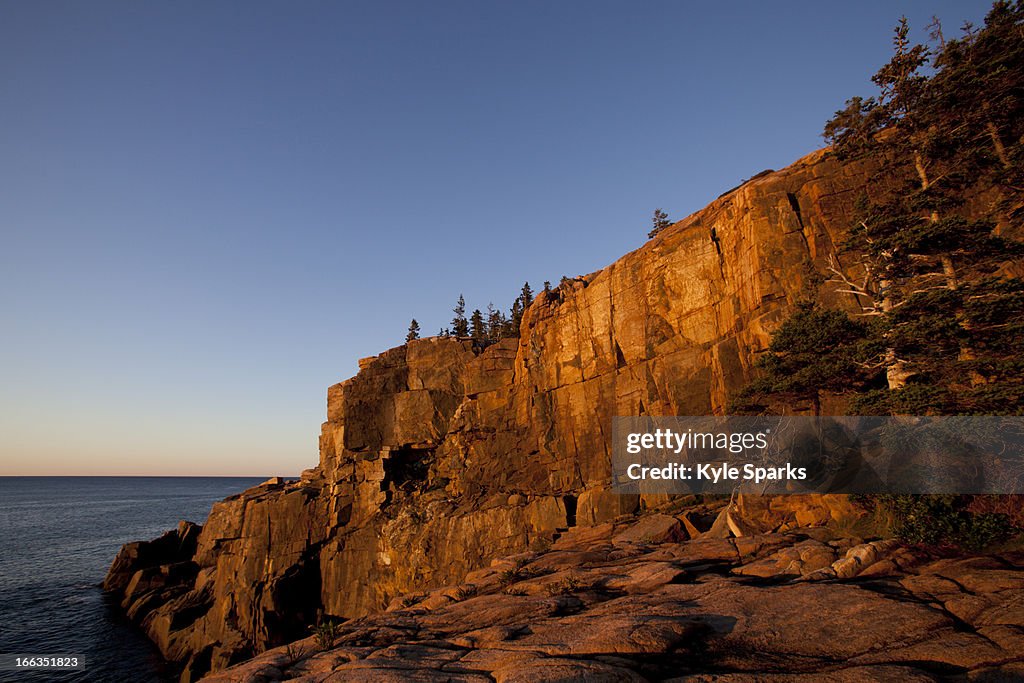 The first rays of sunshine light up the Otter Cliffs located in Acadia National Park near Bar Harbor, Maine.