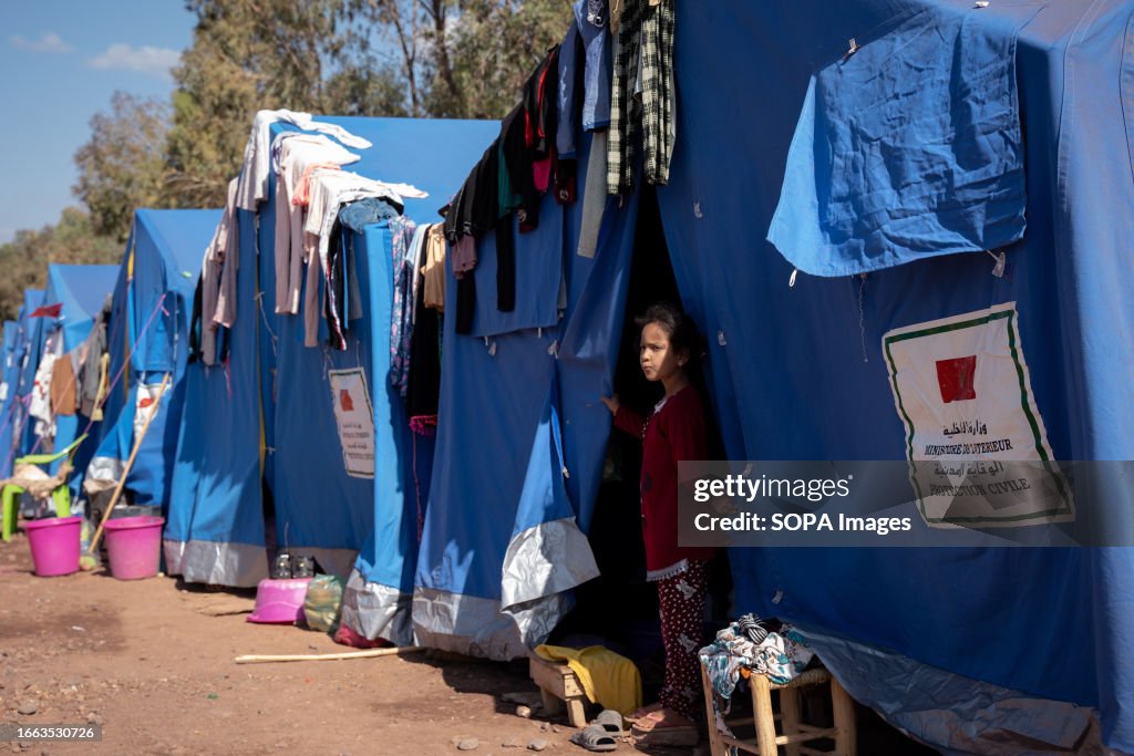A girl is seen standing outside a tent serving as a...