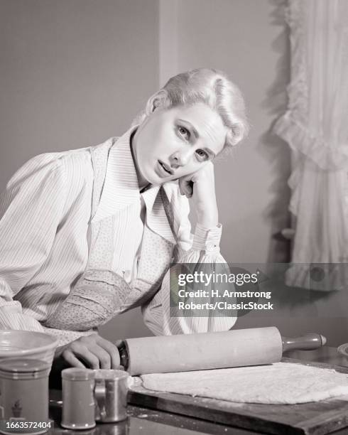 1940s 1950s disgruntled attractive blonde woman housewife looking at camera in kitchen rolling out pie crust dough.