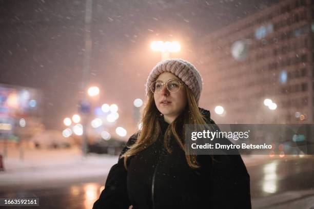 young woman walking on the street in the city during snowfall in winter at night - woman snow outside night stockfoto's en -beelden
