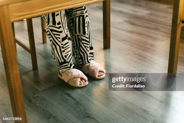 women's legs in pajama pants and house fluffy slippers. morning in the kitchen, at breakfast, work at home, sick leave, depression, apathy concept. home cozy - slipper stock pictures, royalty-free photos & images