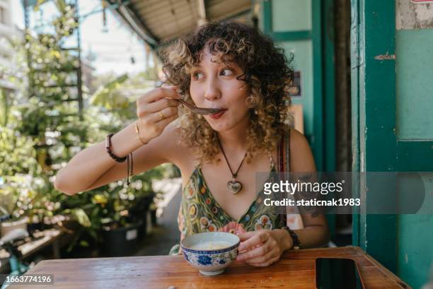 cheerful woman who sitting in front of restaurant enjoying eating tasty thai dessert. - tasty stock pictures, royalty-free photos & images