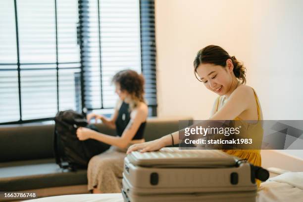 two young asian women stay in their room and pack their clothes in suitcases before heading off to next destination. - intellectual ventures stock pictures, royalty-free photos & images