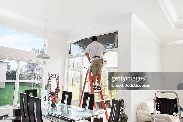 workman on ladder adding tinting to upper, interior window - toned image stock pictures, royalty-free photos & images