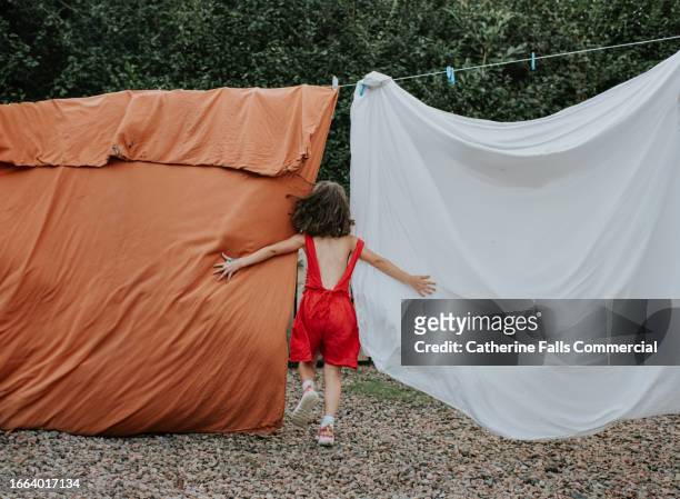 a playful little girl runs between bedsheets hanging on a washing line - tumble dryer sheets stock pictures, royalty-free photos & images