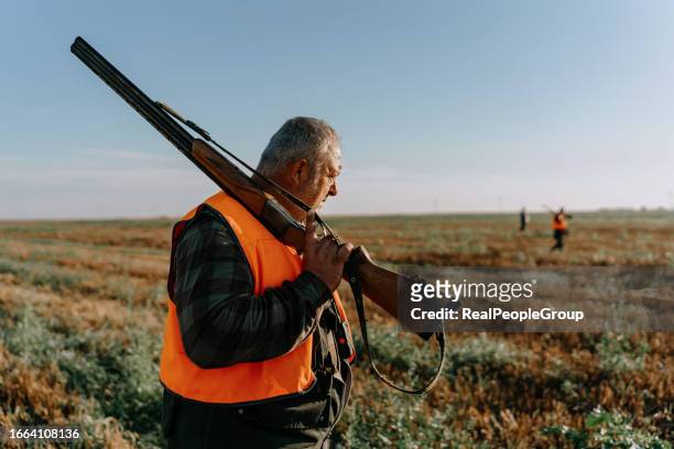a mature caucasian male hunter standing with a shotgun over his shoulder - jachtgeweer stockfoto's en -beelden