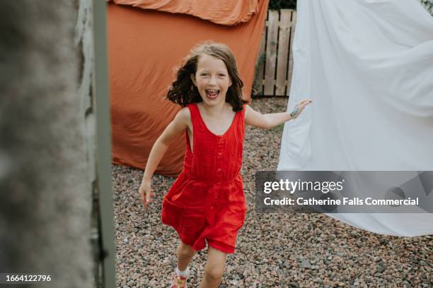 a playful little girl runs between bedsheets hanging on a washing line - tumble dryer sheets stock pictures, royalty-free photos & images