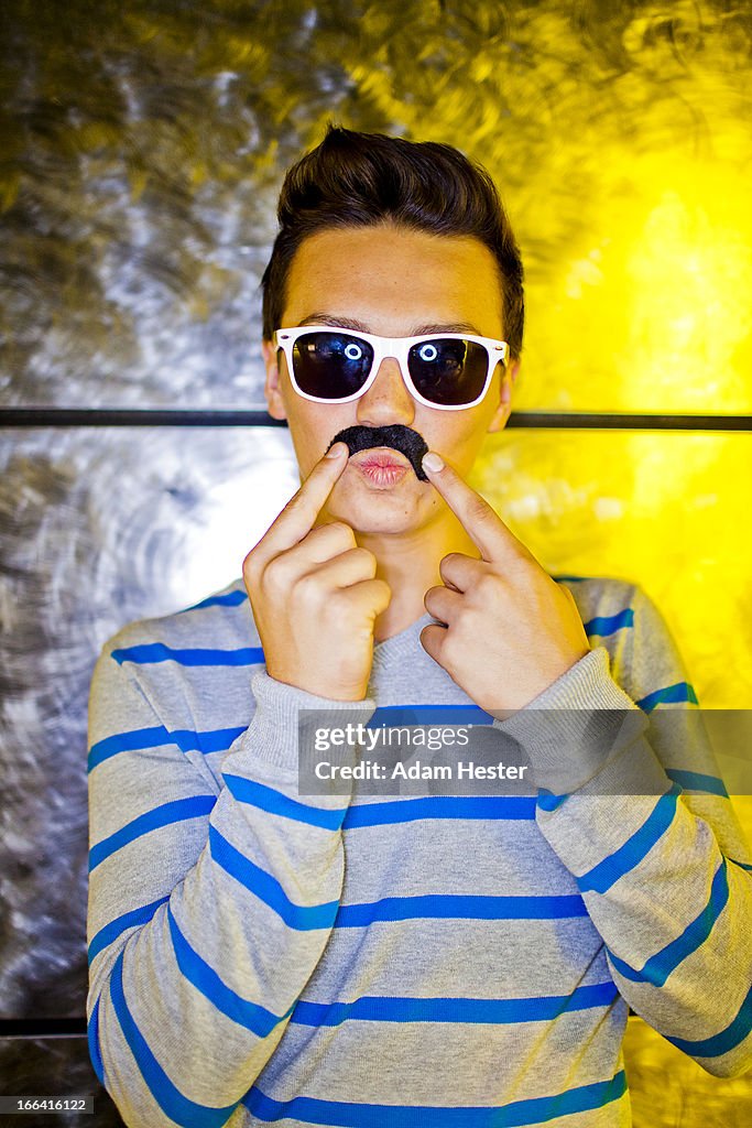 A young man wearing a fake mustache inside.