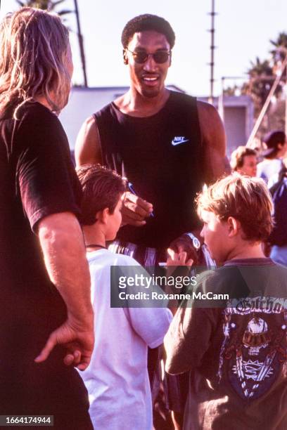Scottie Pippen of the Chicago Bulls signs autographs for young fans while wearing a Nike tank top, black and white pants, a watch and sunglasses on...
