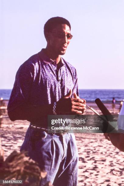 Scottie Pippen of the Chicago Bulls speaks into a microphone wearing sunglasses, a blue collared shirt, jeans, a silver bracelet, and a silver and...
