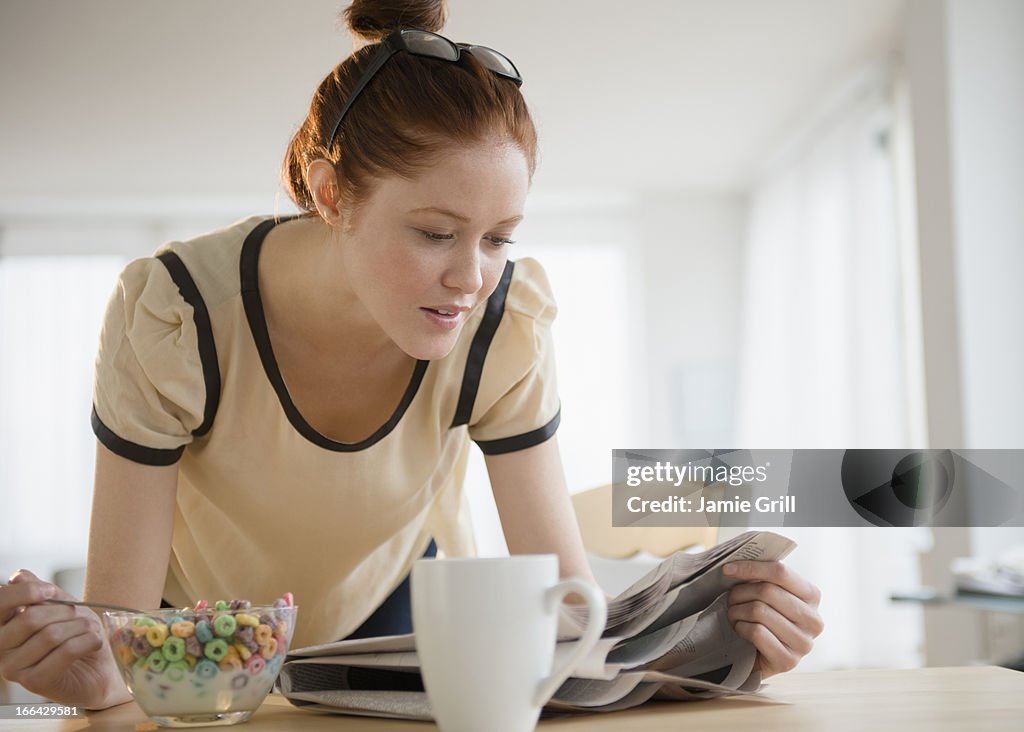 Woman eating cereal while reading newspaper