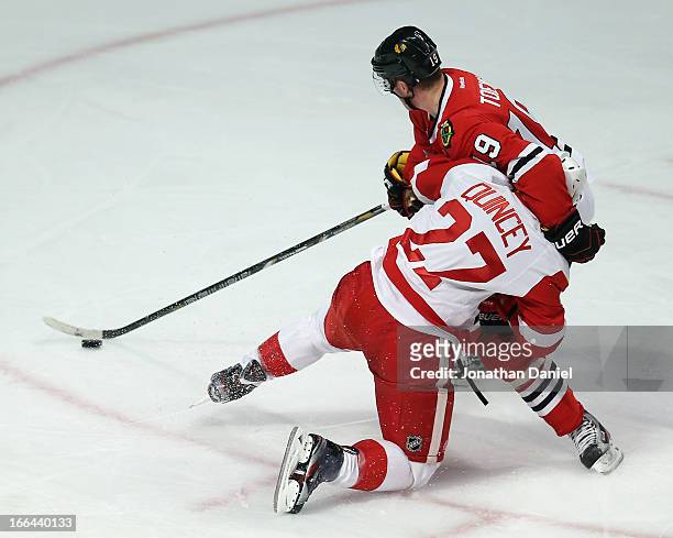 Jonathan Toews of the Chicago Blackhawks holds off Kyle Quincey of the Detroit Red Wings with one arm as he advances the puck at the United Center on...