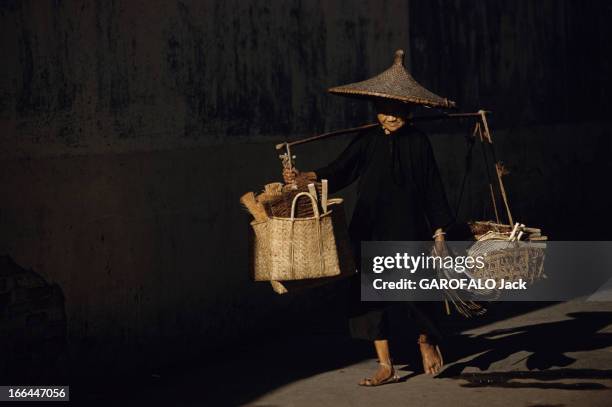 The District Of Cholon In Saigon , Vietnam. Saigon - 1961 - Dans une rue du quartier chinois de Cholon, une personne vêtu de noir, avec un chapeau...