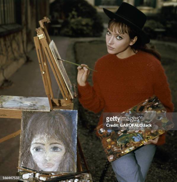 Rendezvous With Anna Karina. Paris - Juin 1964 - Dans son jardin du Trocadéro, devant un chevalet, portant un pull rouge et un chapeau noir,...