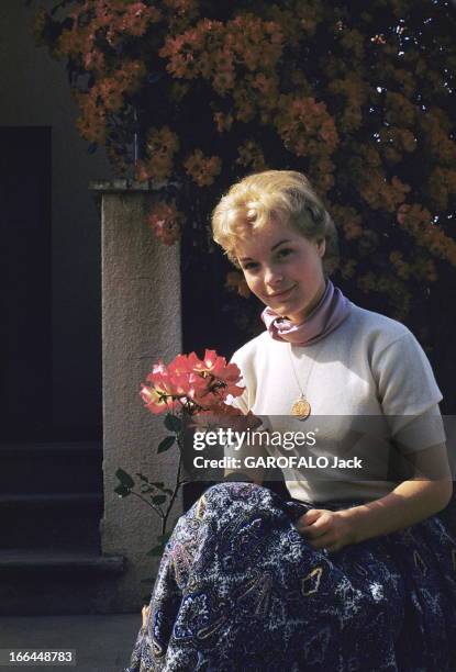 Rendezvous With Romy Schneider, 19 Years Old, In Cannes. Attitude souriante de Romy SCHNEIDER assise devant un mur de fleurs rouges, une fleur à la...
