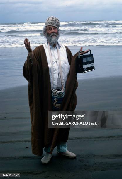 Campaigns Of Iran. En Iran, en 1969, sur une plage, dos à la mer, un homme barbu coiffé d'un bonnet brodé, levant les mains en tenant un poste de...