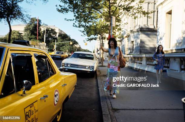 New York, United States. New York - août 1971 - Dans une rue, une femme vêtue d'une chemisette nouée sous la poitrine et d'une jupe fendue en...