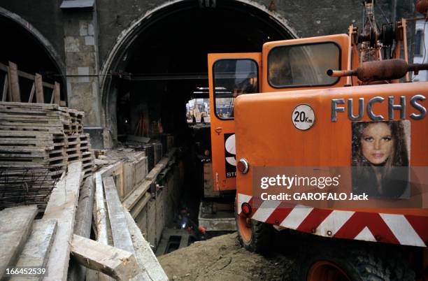 Munich And Leverkusen In Germany. Munich - décembre 1968 - Une pelleteuse orange sur un chantier de la ville, devant un bâtiment en arcades.