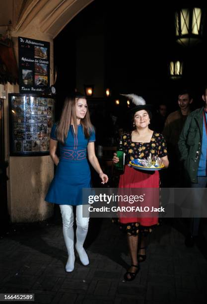 Munich And Leverkusen In Germany. Munich - décembre 1968 - Dans une brasserie, une femme en robe bleue et cuissardes blanches, en compagnie d'une...