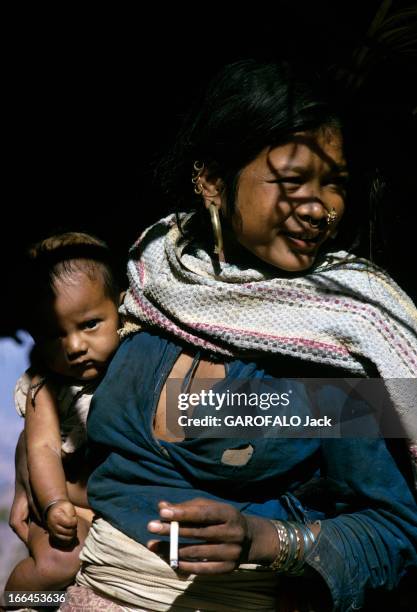 Nepal. Népal- mars 1970- Paysanne portant des anneaux et bijoux au nez et oreilles, cigarette en main, son enfant sous son bras.