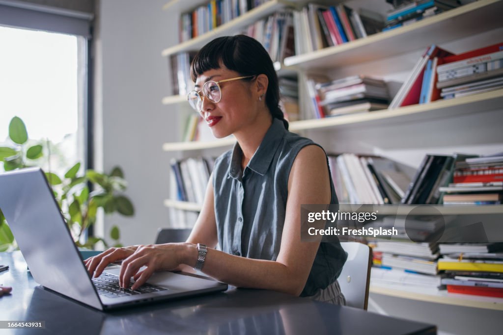 A Happy Beautiful Asian Businesswoman With Glasses Using Her Computer While Working In The Office