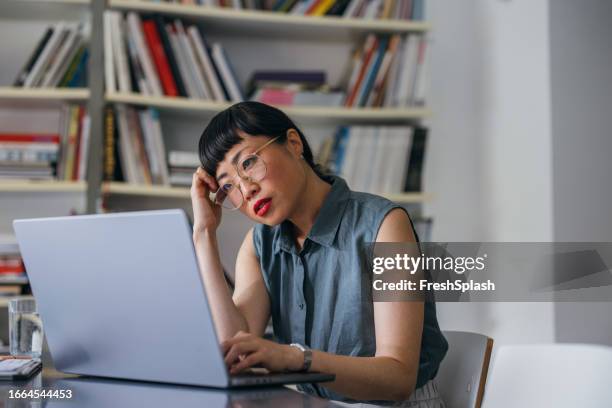 a frustrated beautiful asian businesswoman with glasses using her computer while working in the office - japanese people laptop unhappy stock pictures, royalty-free photos & images