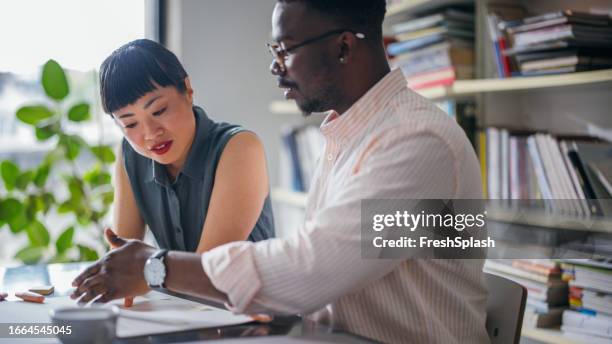 zwei kollegen, die sich unterhalten, während sie zusammen im büro arbeiten - african american mentor stock-fotos und bilder