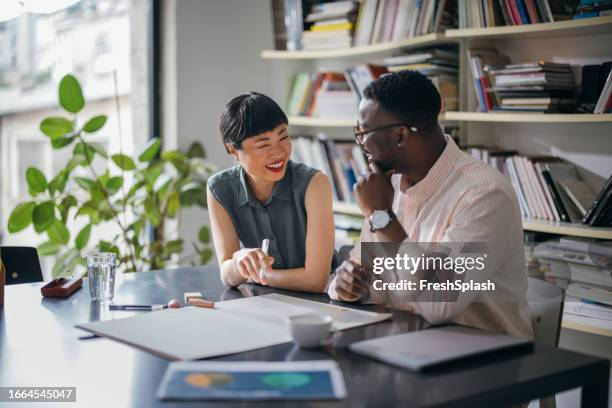 two happy colleagues talking while working together in the office - onderhandelen stockfoto's en -beelden