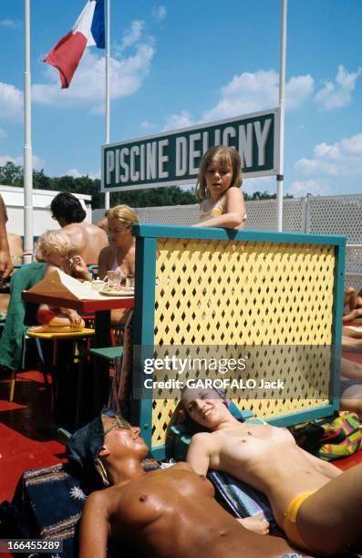 Topless At The Pool Deligny. Paris - mars 1973 - Une fillette observant deux femmes bronzant les seins nus, allongée sur des serviettes au solarium...