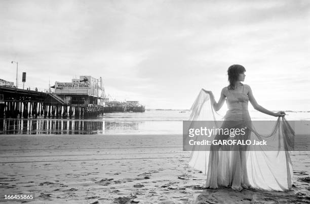 Communities In California. Etats-Unis, Californie, Santa Monica, janvier 1971, ici sur la plage, une femme écarte les pans de sa robe longue pour...