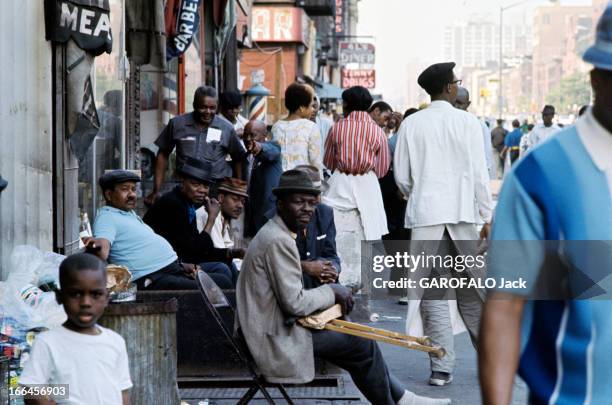 New York, United States. New York - août 1971 - Dans une rue, un groupe d'hommes afro-américains, dont un tenant des béquilles de bois sur ses...
