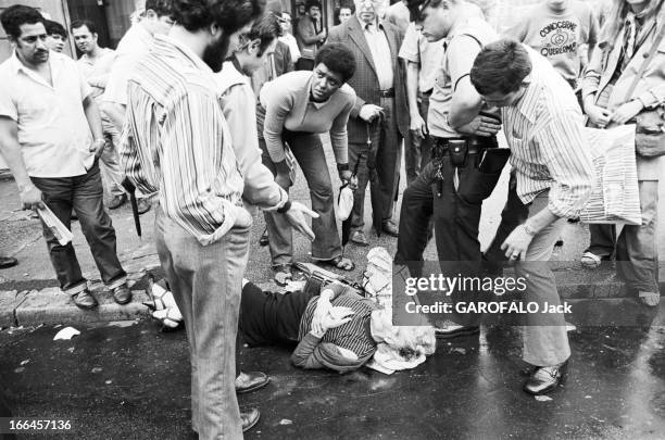 New York, United States. New York - août 1971 - La vie quotidienne dans les quartiers de la ville. Un policier et des passants autour d'une femme...