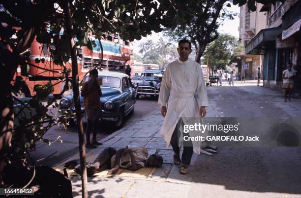 Jesuits In India. En Inde, en mai 1973, dans une rue, le père jésuite Sydney D'SOUZA en tunique blanche, passant à côté d'un homme allongé sur une...