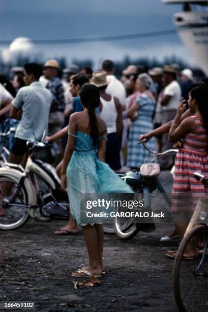 Tahiti In July. Tahiti - juillet 1959 - A l'occasion des festivités du 'Juillet', sur le port, une femme de dos en robe bleue, devant un groupe de...