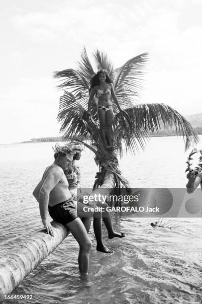 Elles Et Eux ' In Tahiti. En 1961, 'ELLES et EUX' à TAHITI . Assis sur le tronc d'un palmier, un homme non-identifié et une tahitienne trempent les...