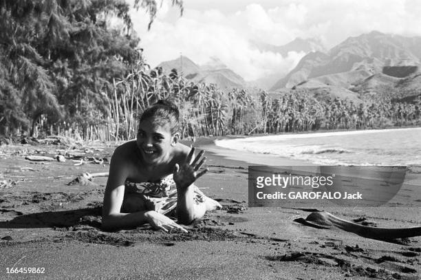 French Polynesia. Le 29 décembre 1959, à Tahiti en Polynésie française, l'ile au quotidien : une femme en paréo couchée sur le sable, saluant...