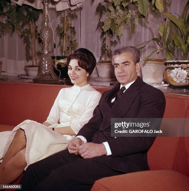 The Shah Of Iran In His Palace. Téhéran - 1959 - Dans le Palais Royal, assis sur un canapé rouge, souriants, l'impératrice D'IRAN Farah DIBA, en robe...