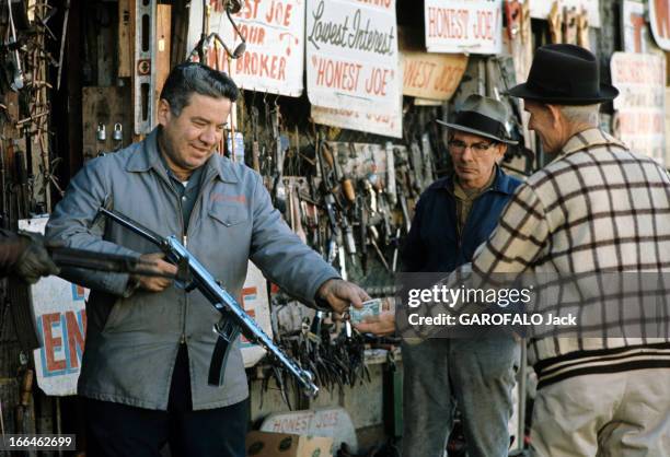 Dallas, Texas Capital. Dallas - décembre 1963 - Dans une rue de la ville, deux hommes devant la vitrine de l'armurerie 'Honest Joe', dont un tenant...