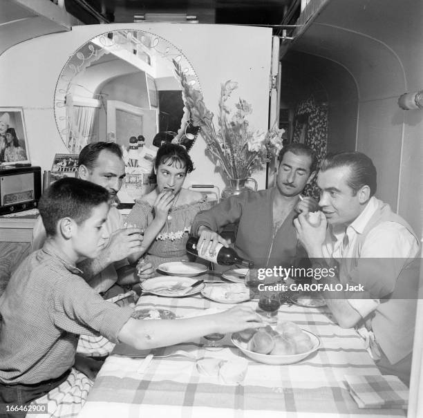 Circus Achille Zavatta. La troupe d'Achille ZAVATTA lors d'une tournée : ici assis à une table , dans une roulotte, en famille, se servant du vin,...