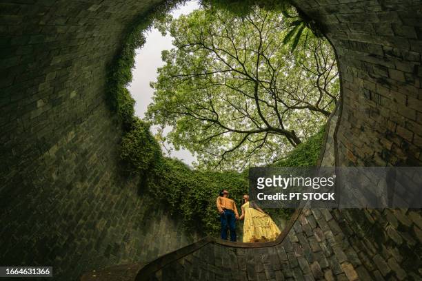 men and women, fort canning tree tunnel, singapore. on a rainy day, a popular place for tourists to take pictures is the tunnel-like structure covered with green trees. - fortress gate and staircases stockfoto's en -beelden