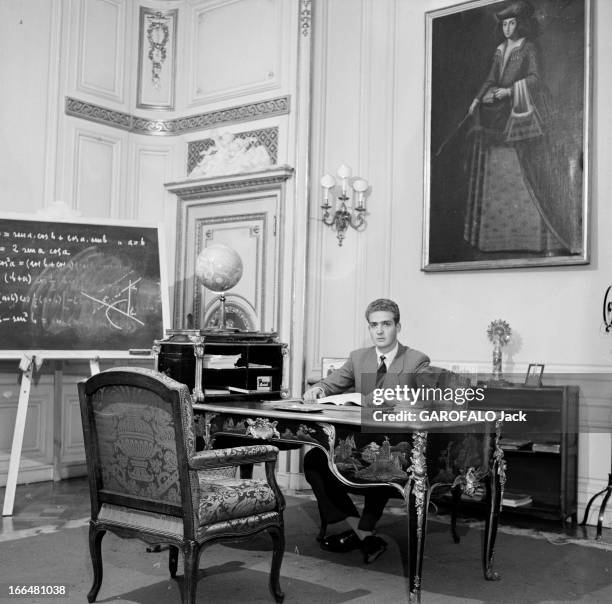 Don Juan Carlos Ist Of Spain. Espagne- période 1955-1958- Juan CARLOS IER D'ESPAGNE, en costume, assis à son bureau, un globe terrestre et des livres...