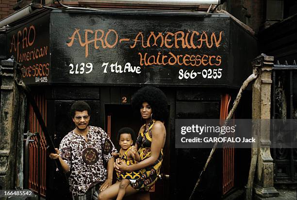 The Ghetto. New York City- Harlemle ghetto; une jeune femme afro-américaine, portant une perruque 'dernier cri' porte son enfant coiffé d'une...