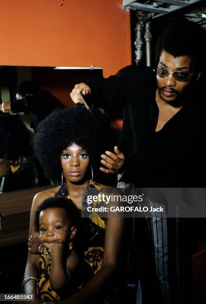 The Ghetto. New York City- Harlemle ghetto; le coiffeur et sa cliente, assise, tenant son enfant dans le salon de coiffure.